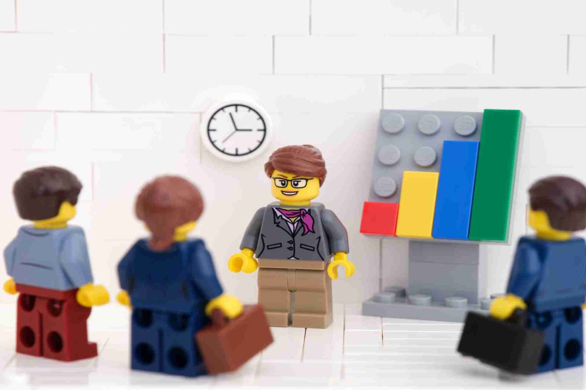 LEGO figures in a business meeting, with one figure presenting a bar chart while others listen, briefcases in hand