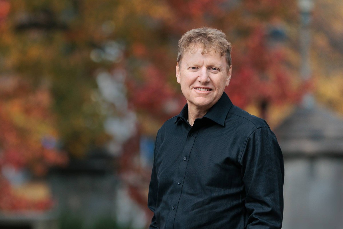 Man smiling outdoors with autumn leaves in the background