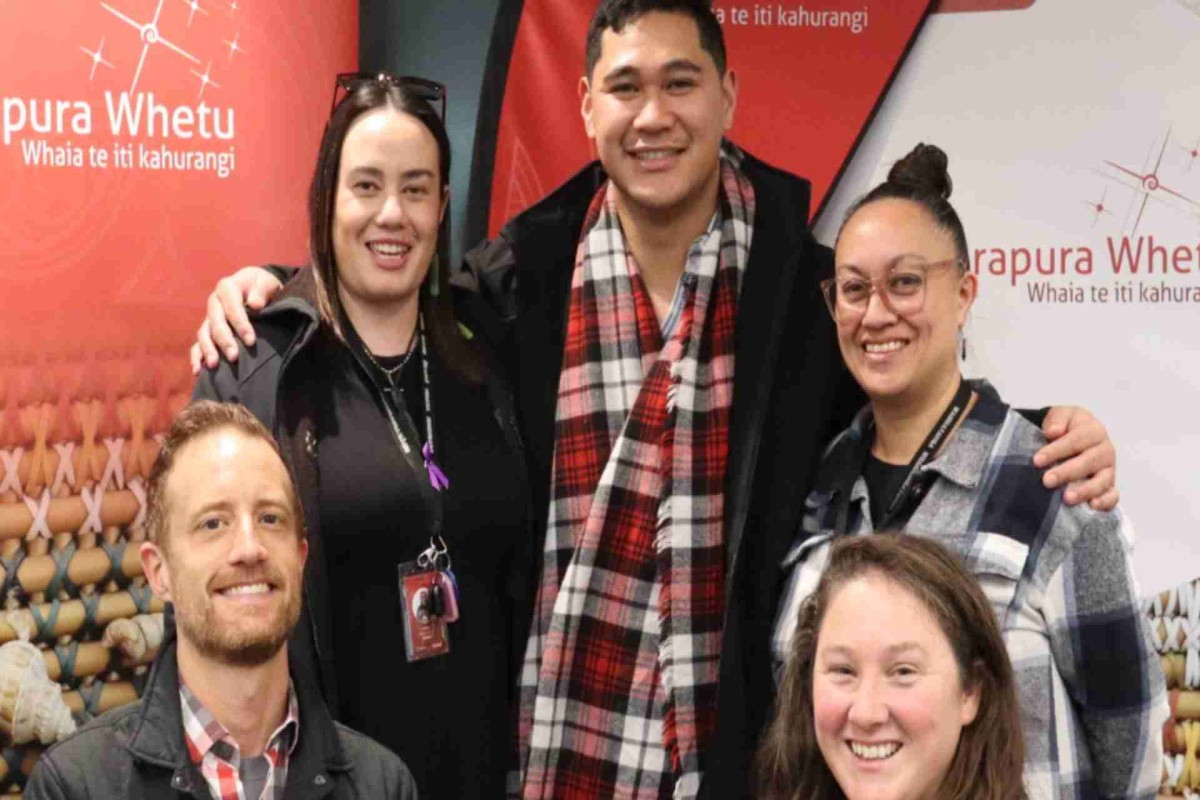 Group of five people smiling together in front of Purapura Whetū banners