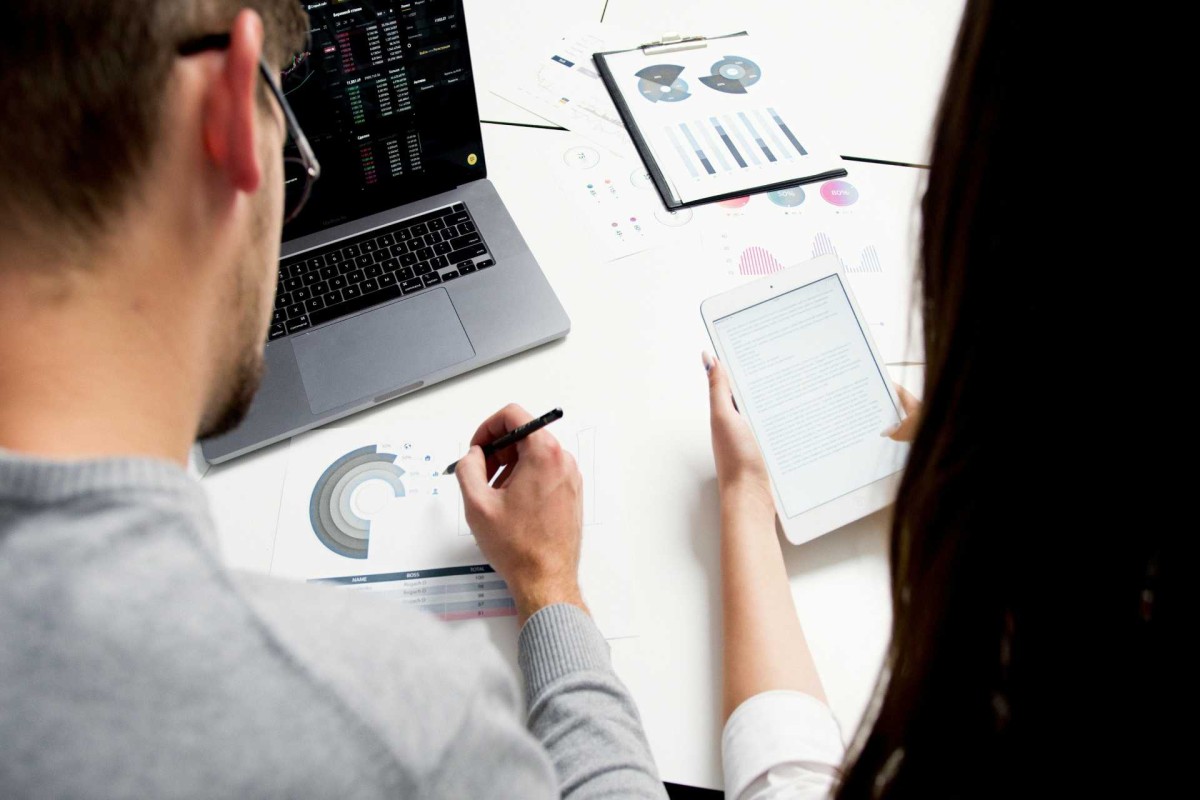 Two people reviewing business charts and data on a laptop and tablet