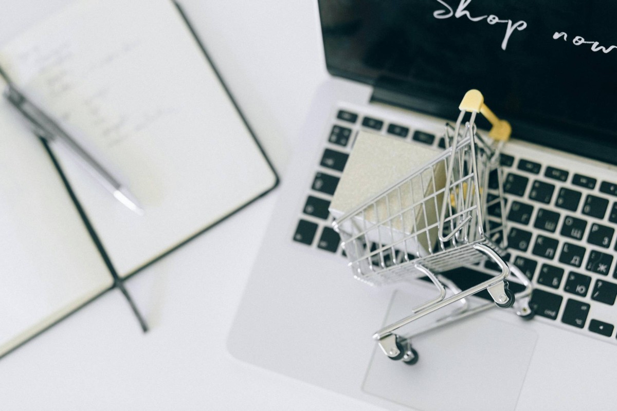 A small shopping cart placed on a laptop keyboard beside an open notebook and pen