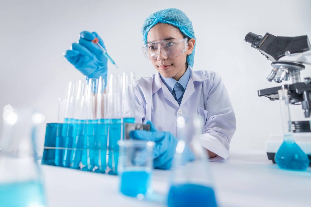 A scientist wearing protective gear carefully handling blue liquid samples in a lab.