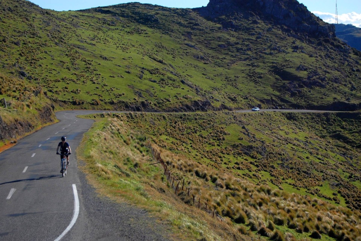 Cyclist riding along a winding road through green hills near Christchurch