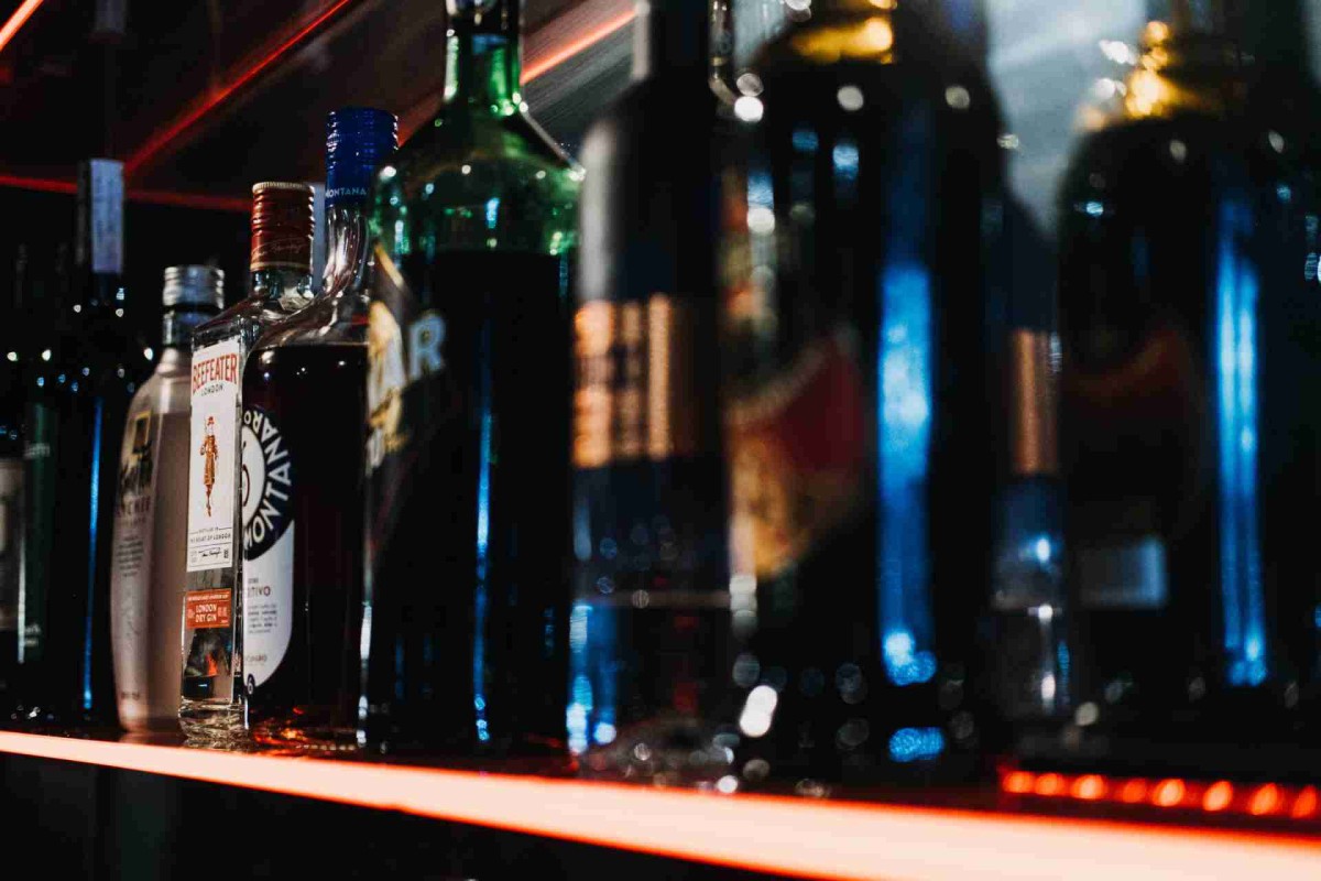 Assorted liquor bottles lined up on a dimly lit bar shelf with red lighting