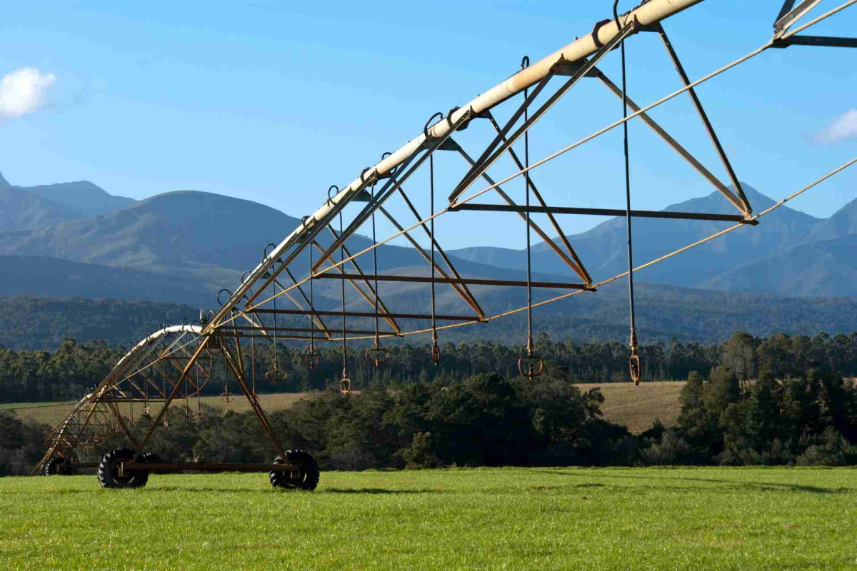 Large center pivot irrigation system spraying water across a grassy agricultural field with mountains in the background