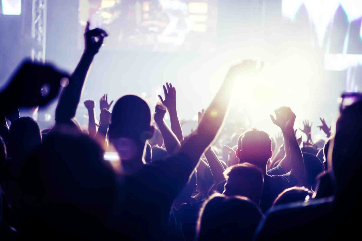 A large crowd with raised hands enjoying a brightly lit live music concert.