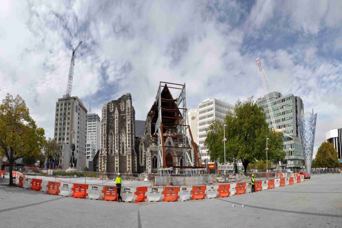 Damaged stone church under reconstruction with cranes and fencing in a city square