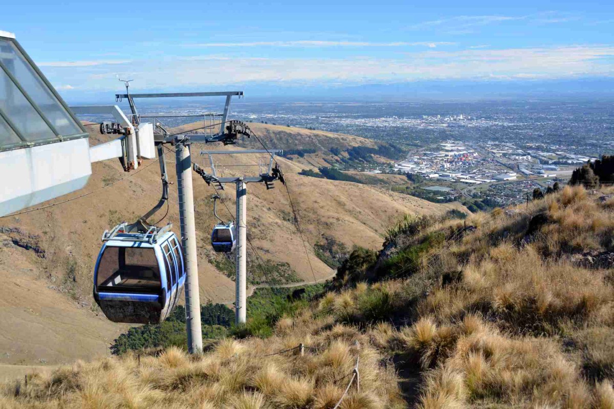 Cable car gondola traveling up a dry grassy hillside with Christchurch city and plains visible in the distance.