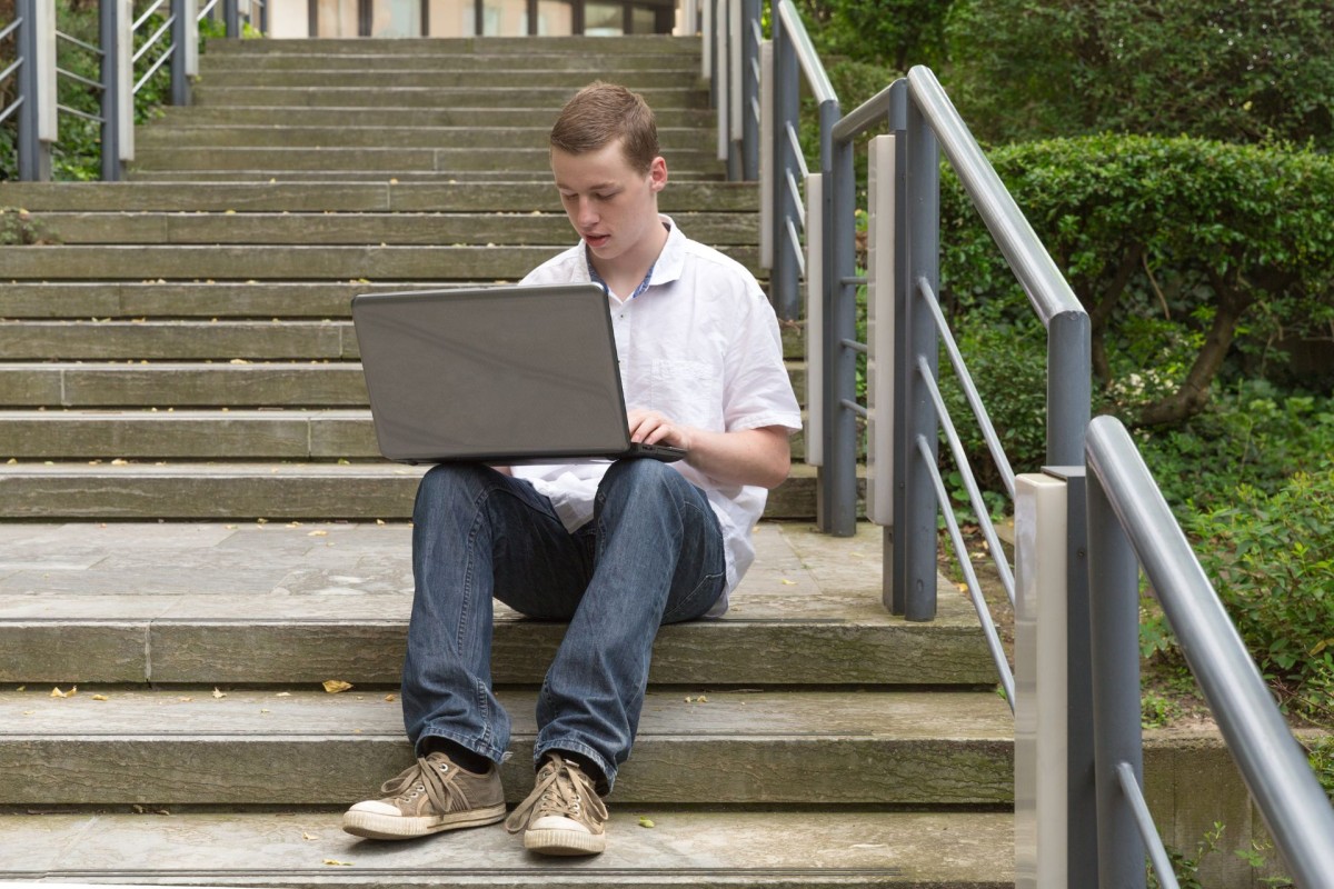 A young guys sitting on a concrete stairs working on his laptop