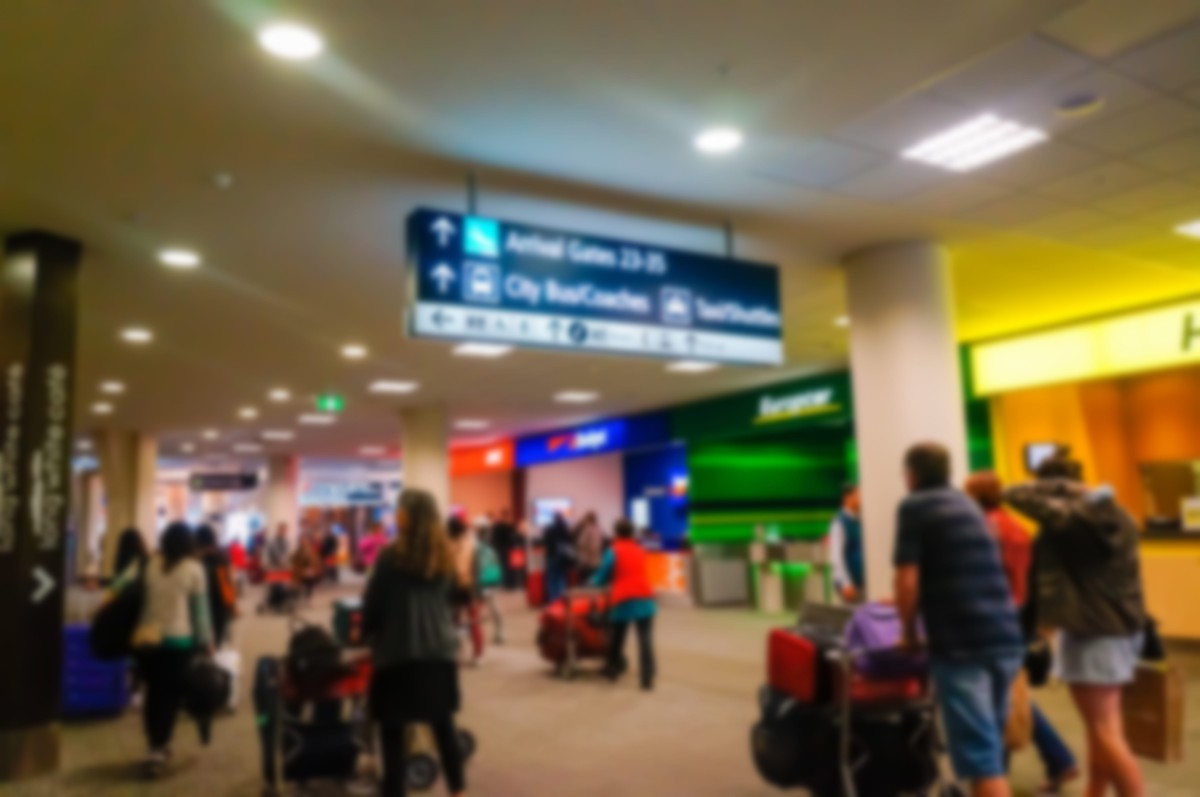 Busy airport terminal with travelers walking and pushing luggage under overhead directional signs