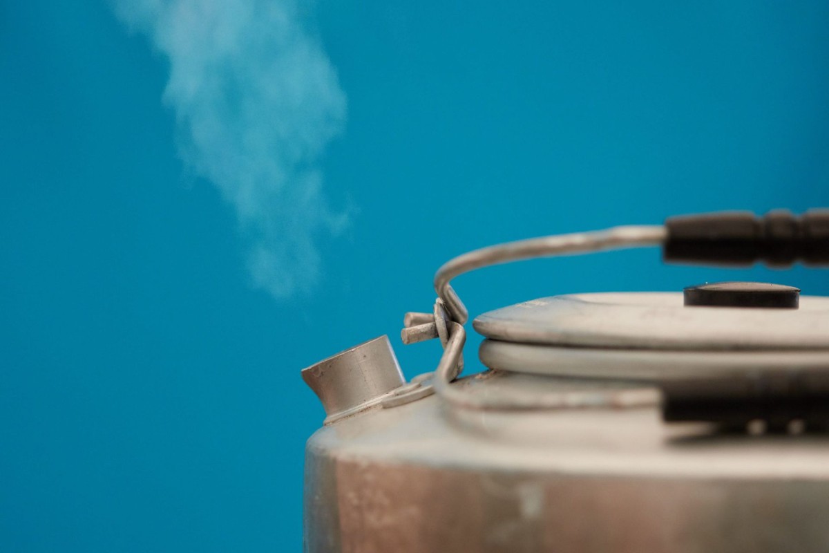 Steaming metal kettle against blue background.