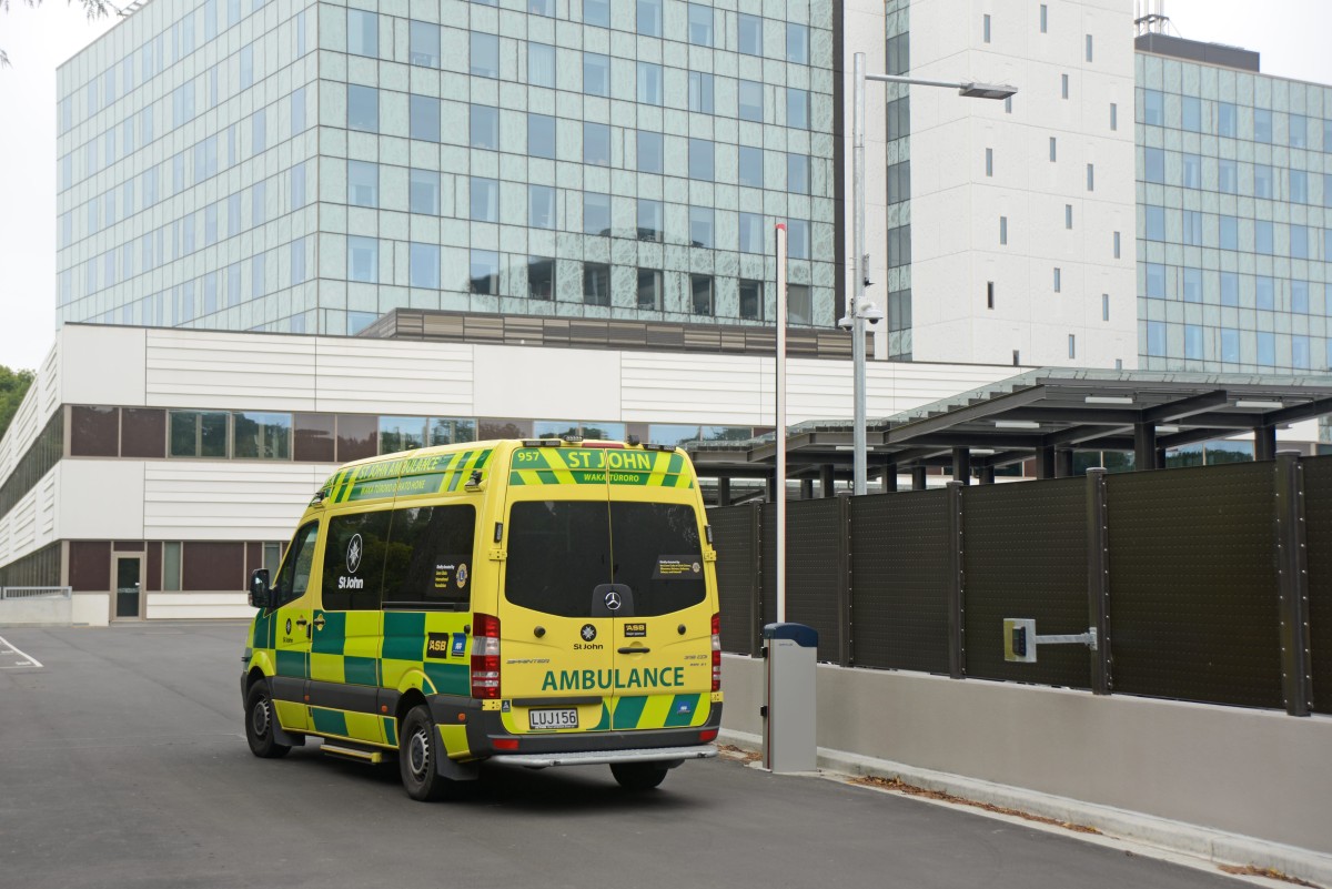Green and yellow ambulance driving near a hospital entrance