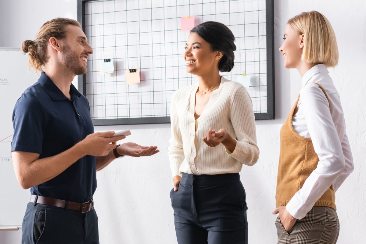 Three smiling coworkers talking in a modern office.