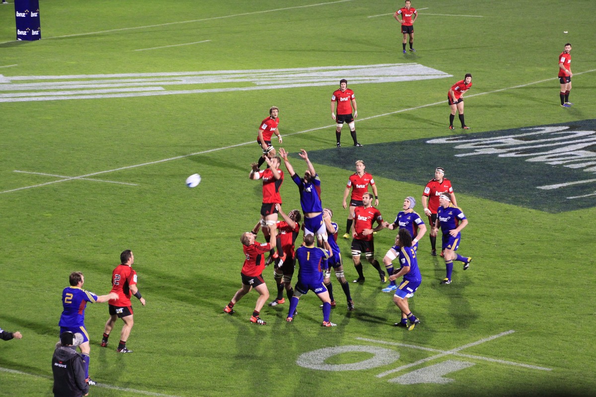 Rugby players from two teams jumping to catch the ball during a lineout on a grass field