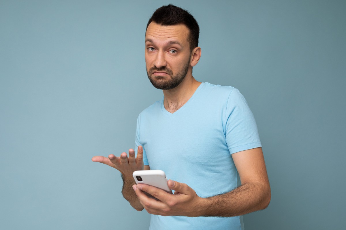 Man holding a phone with a confused, unimpressed expression and one hand raised