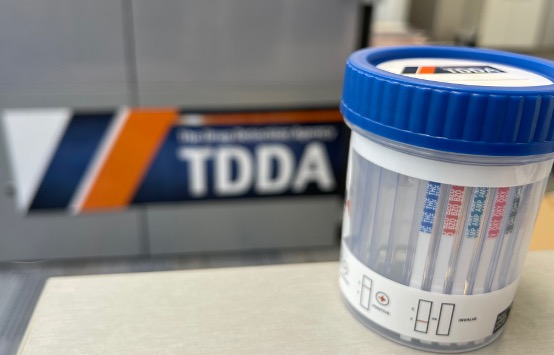 A TDDA drug testing cup with the company logo in the background