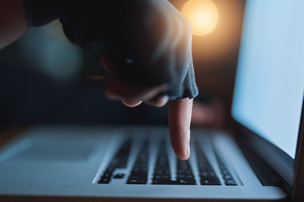 Gloved finger pointing at a computer keyboard in dim lighting, symbolising cybersecurity threats and online scams
