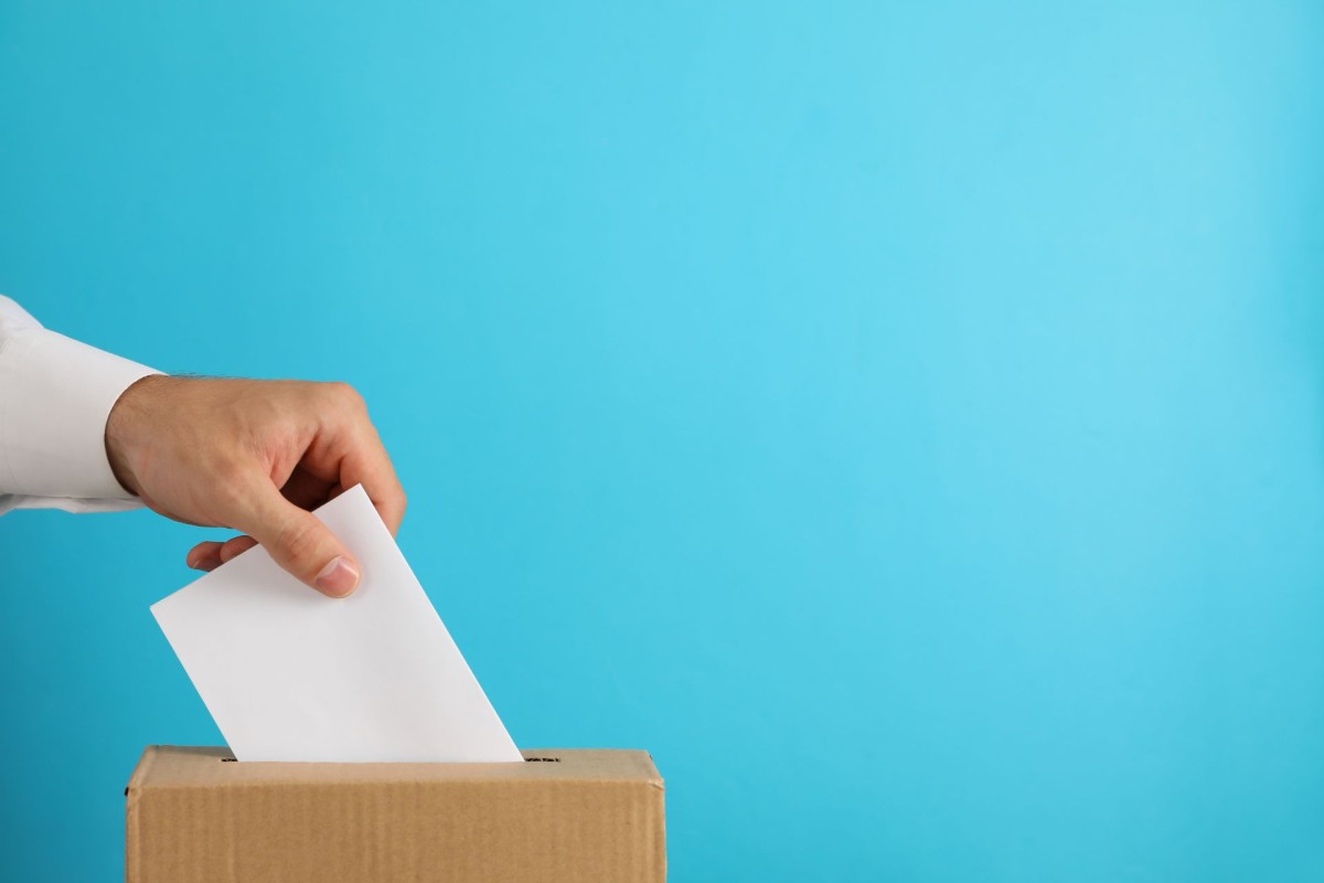 Hand placing a white envelope into a cardboard ballot box for election voting