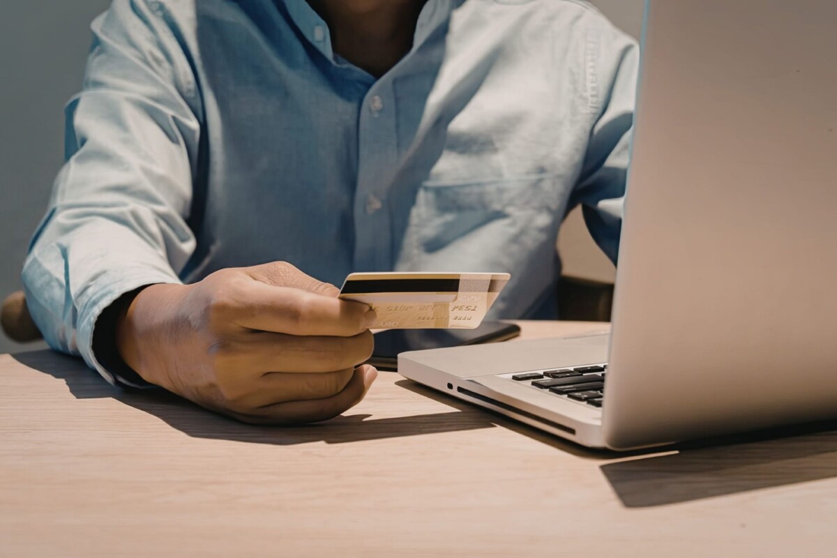 Person holding a debit or credit card beside a laptop while preparing to make an online payment.