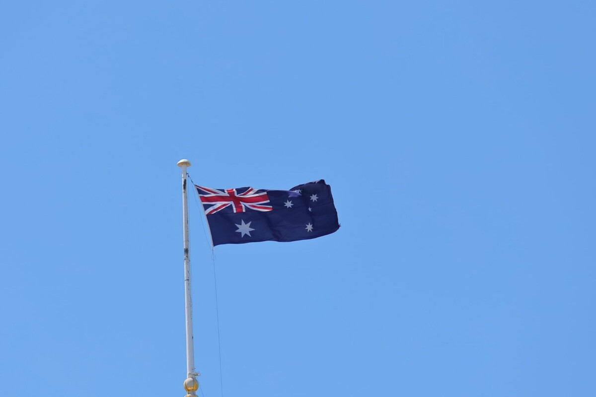 Australian flag flying on a flagpole against a clear blue sky.