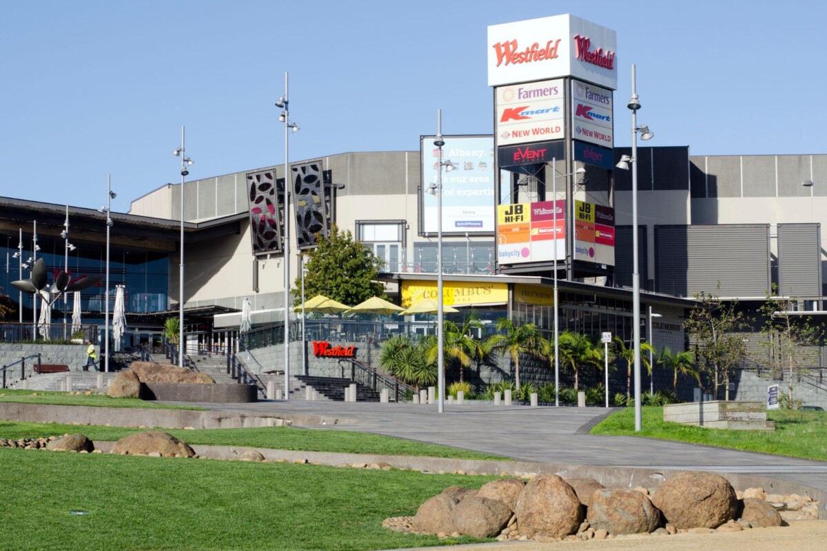 Westfield shopping centre in Albany, Auckland, featuring its multi-storey retail complex, prominent tenant signage, landscaped grounds and outdoor pedestrian areas.